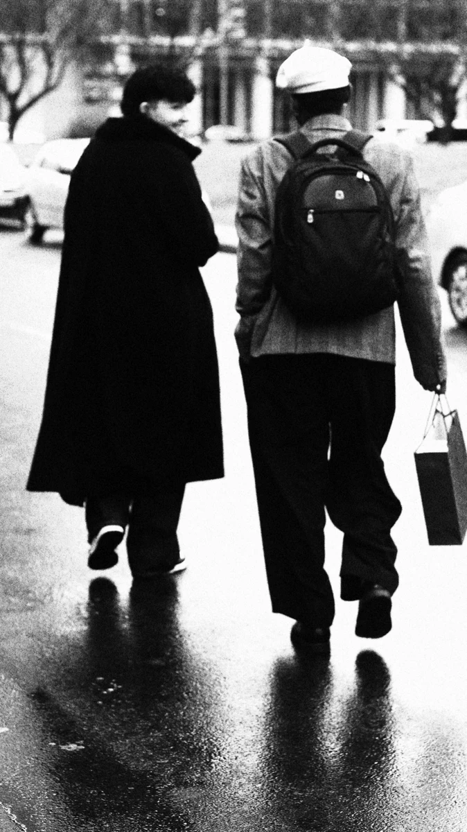 Two figures walking on a wet street, photographed in black and white