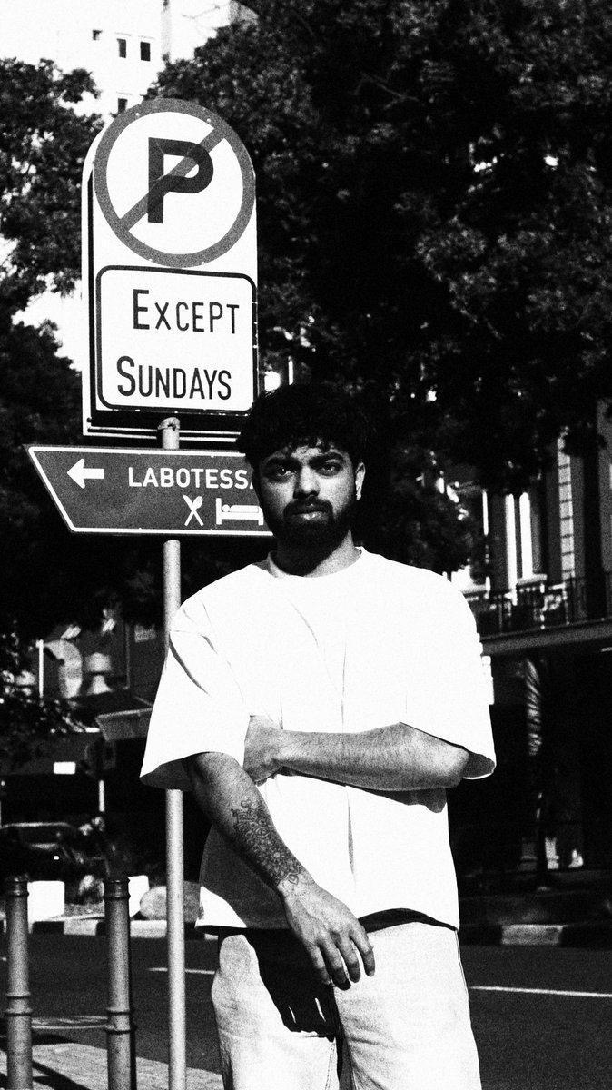 Subject leaning against a street sign in black and white