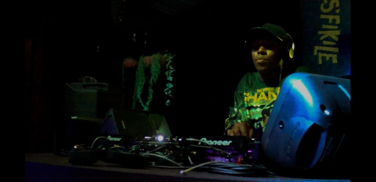 DJ on stage behind Pioneer decks, green light cutting through the dark