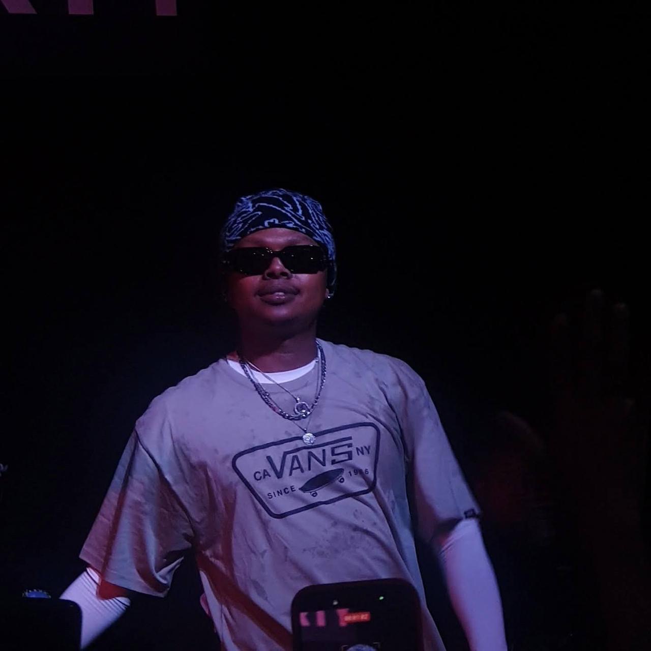 Performer in a Vans tee and durag, framed by purple stage light