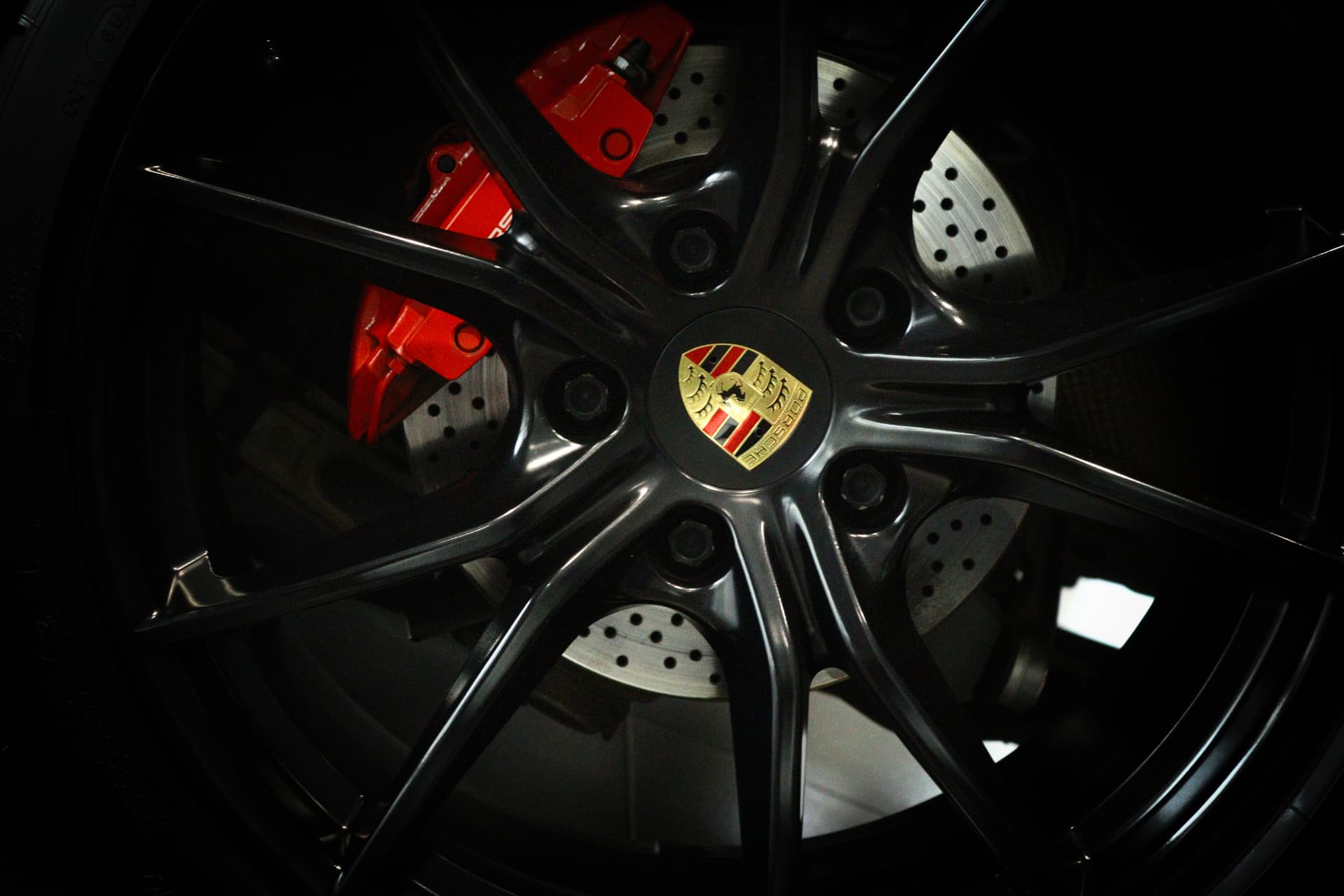 Porsche wheel and red brake caliper behind dark spokes